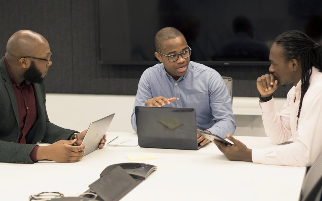 a group of people sitting around a table with laptops